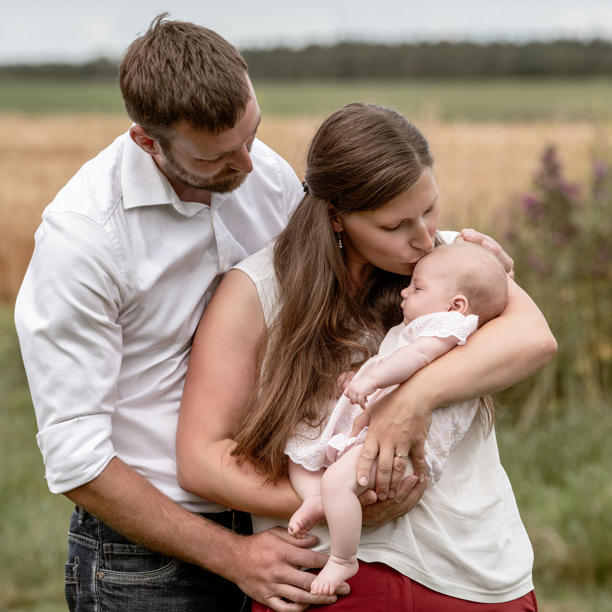 Mutter hält ihr Neugeborenes liebevoll im Arm und küsst das Baby auf die Stirn, während der Vater sich schützend zu beiden neigt.